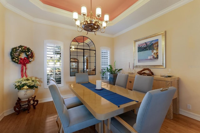 dining space with a raised ceiling, dark hardwood / wood-style flooring, an inviting chandelier, and ornamental molding