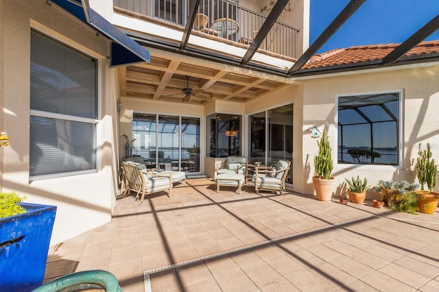 view of patio with glass enclosure, ceiling fan, and a balcony