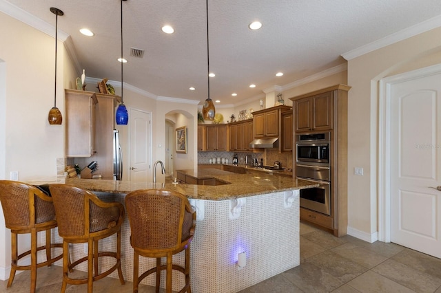kitchen with arched walkways, under cabinet range hood, dark stone countertops, and a peninsula