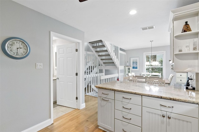 kitchen featuring decorative light fixtures, white cabinetry, light stone countertops, and light hardwood / wood-style flooring