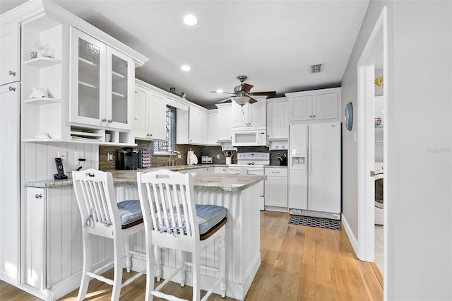 kitchen featuring light stone countertops, light hardwood / wood-style flooring, backsplash, white appliances, and white cabinets