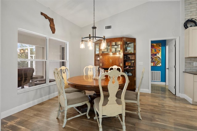 dining area with dark hardwood / wood-style flooring, high vaulted ceiling, and an inviting chandelier