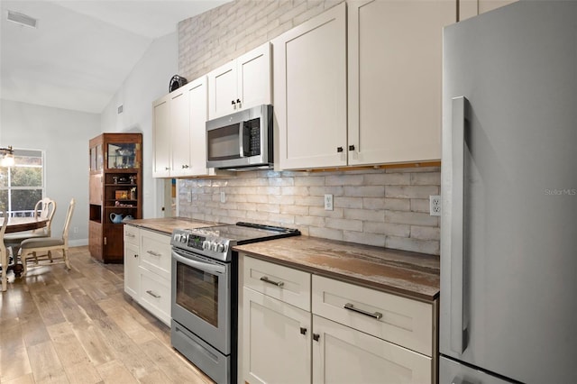 kitchen featuring appliances with stainless steel finishes, tasteful backsplash, light hardwood / wood-style flooring, white cabinetry, and lofted ceiling