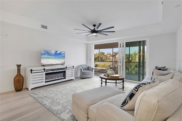 living room with a tray ceiling, ceiling fan, and light wood-type flooring