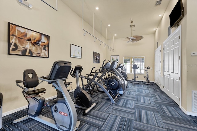 workout area with ceiling fan, a towering ceiling, and dark carpet