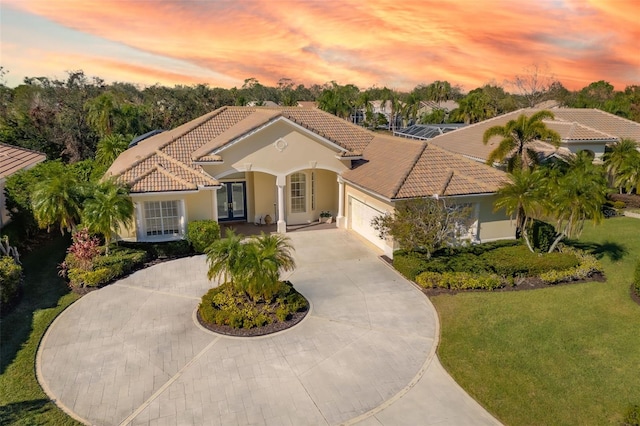 mediterranean / spanish house featuring a front yard, an attached garage, stucco siding, curved driveway, and a tile roof