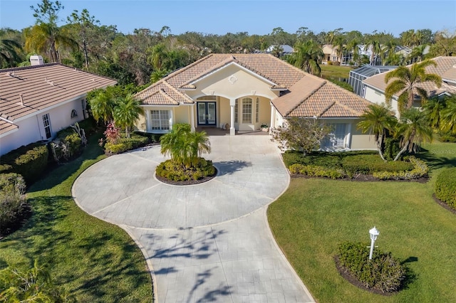 mediterranean / spanish house with a tile roof, stucco siding, a front yard, and curved driveway