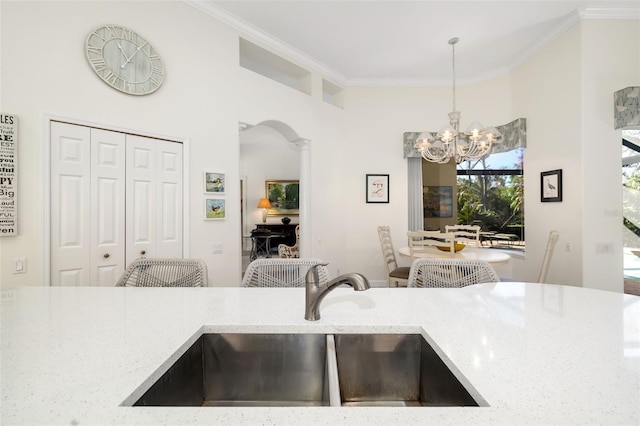 kitchen with a notable chandelier, light stone counters, a sink, crown molding, and hanging light fixtures