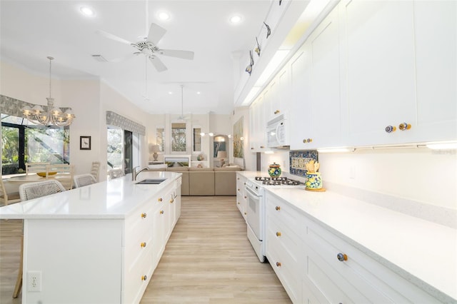 kitchen with open floor plan, light countertops, ceiling fan with notable chandelier, white appliances, and a sink