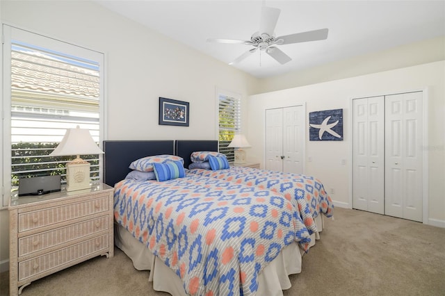 bedroom featuring light colored carpet, baseboards, two closets, and ceiling fan