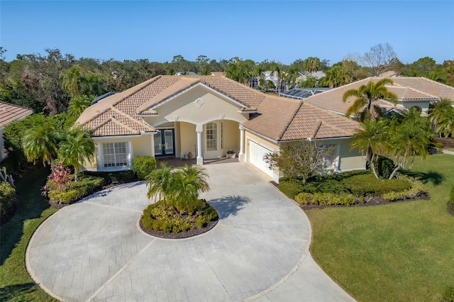 mediterranean / spanish-style house with stucco siding, curved driveway, a front yard, an attached garage, and a tiled roof