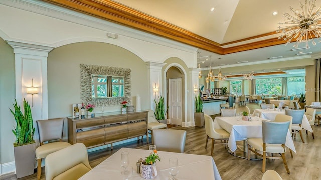 dining room featuring a notable chandelier, ornamental molding, wood finished floors, and decorative columns