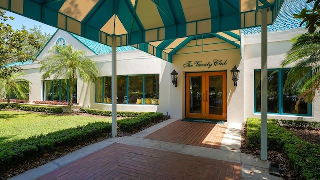 entrance to property with stucco siding, a lawn, and french doors