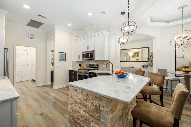 kitchen with white cabinetry, sink, light stone counters, decorative light fixtures, and appliances with stainless steel finishes