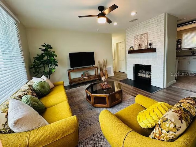 living room featuring dark wood-type flooring, a fireplace, ceiling fan, and plenty of natural light