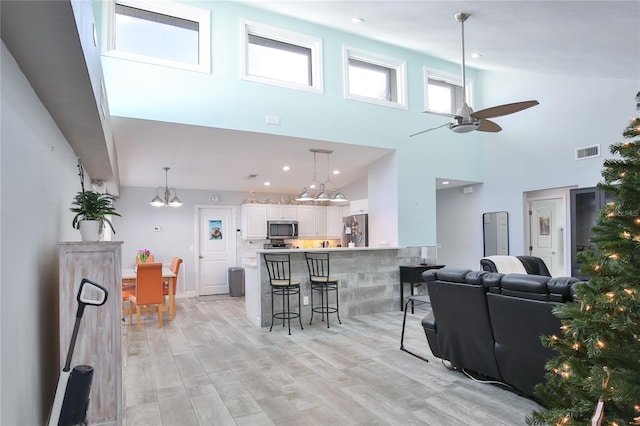 living room featuring ceiling fan with notable chandelier, light hardwood / wood-style floors, and high vaulted ceiling