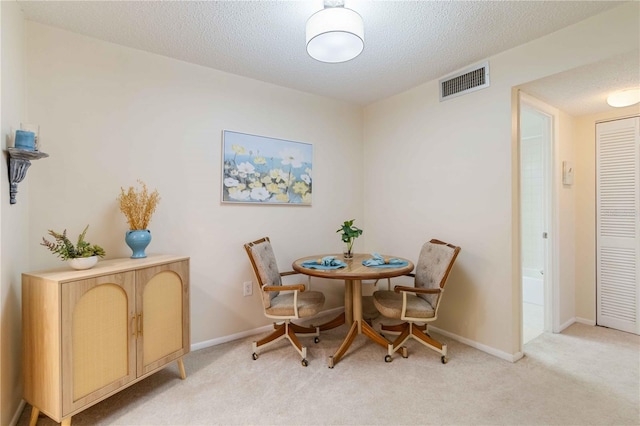 dining area with a textured ceiling and light colored carpet