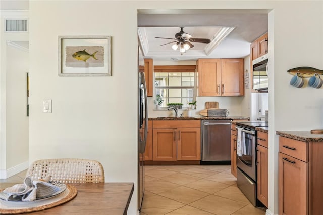 kitchen with sink, ceiling fan, appliances with stainless steel finishes, ornamental molding, and a raised ceiling