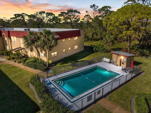 pool at dusk featuring a storage shed and a yard