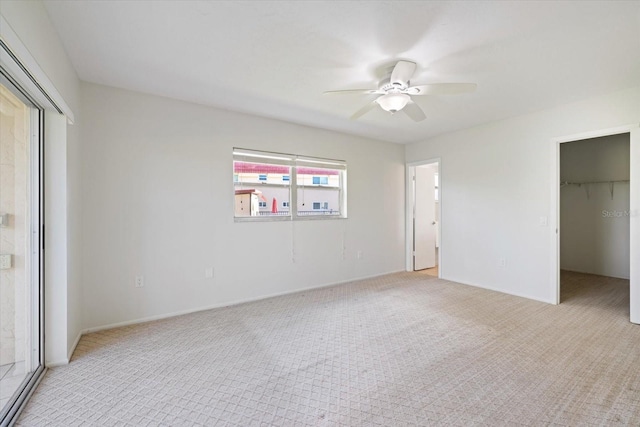 unfurnished bedroom with ceiling fan, a walk in closet, a closet, and light colored carpet