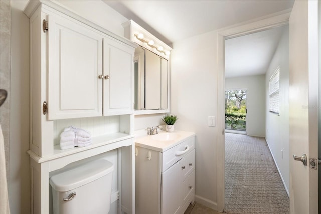 half bath featuring baseboards, vanity, and toilet