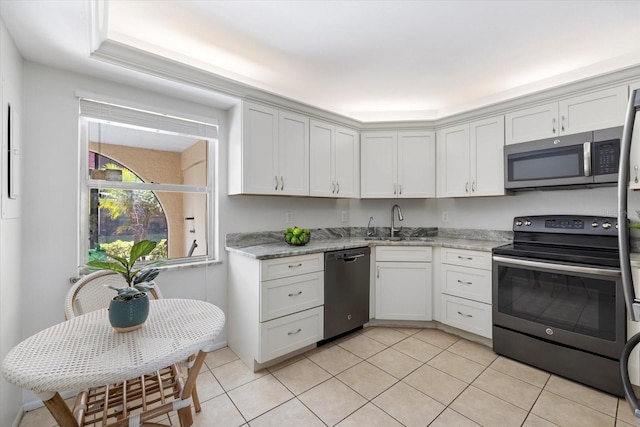 kitchen with light stone counters, light tile patterned flooring, stainless steel appliances, a sink, and white cabinets