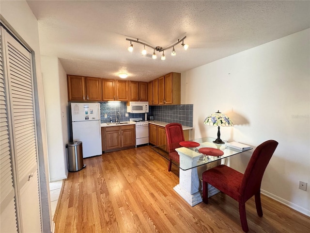 kitchen featuring white appliances, sink, decorative backsplash, a textured ceiling, and light hardwood / wood-style floors