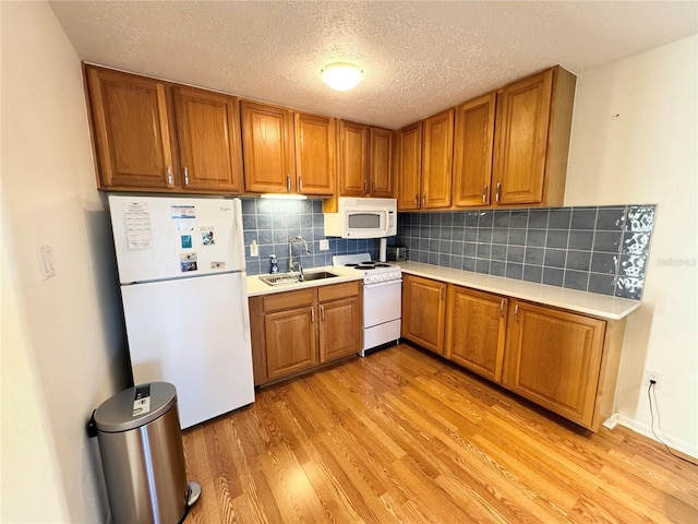 kitchen with sink, tasteful backsplash, a textured ceiling, white appliances, and light wood-type flooring