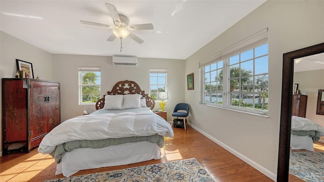 bedroom with ceiling fan, multiple windows, a wall unit AC, and light hardwood / wood-style flooring