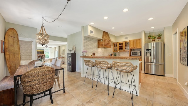 kitchen with pendant lighting, ceiling fan with notable chandelier, decorative backsplash, appliances with stainless steel finishes, and kitchen peninsula