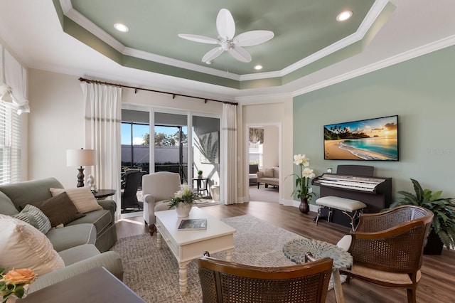 living room with a raised ceiling, dark wood-type flooring, and ornamental molding