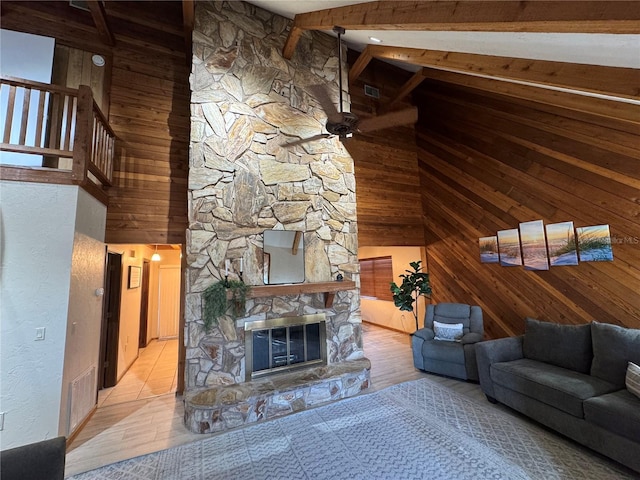 living room with light wood-type flooring, wooden walls, high vaulted ceiling, beamed ceiling, and a stone fireplace