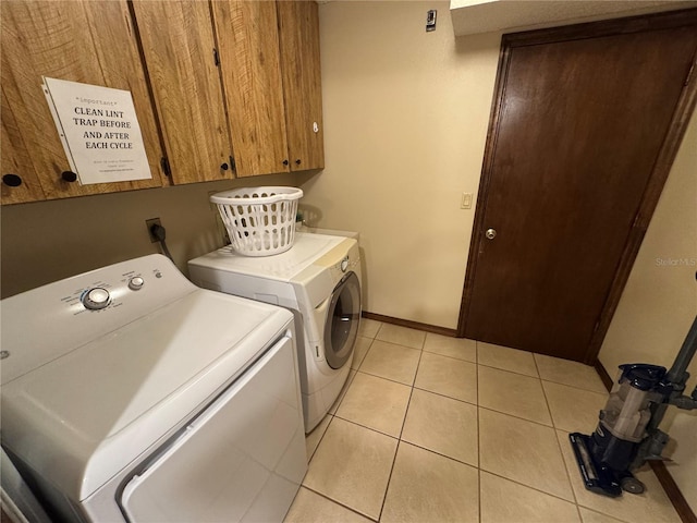 laundry area featuring washer and clothes dryer, light tile patterned floors, and cabinets