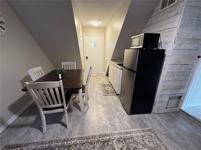 kitchen featuring light wood-type flooring, stainless steel fridge, a textured ceiling, and white cabinetry