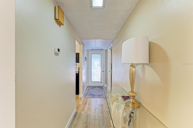 hallway with a textured ceiling and light hardwood / wood-style flooring