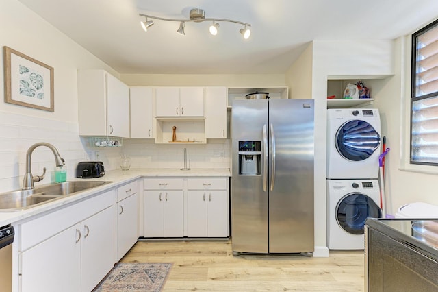 kitchen featuring sink, stainless steel appliances, stacked washer / dryer, light hardwood / wood-style floors, and white cabinets