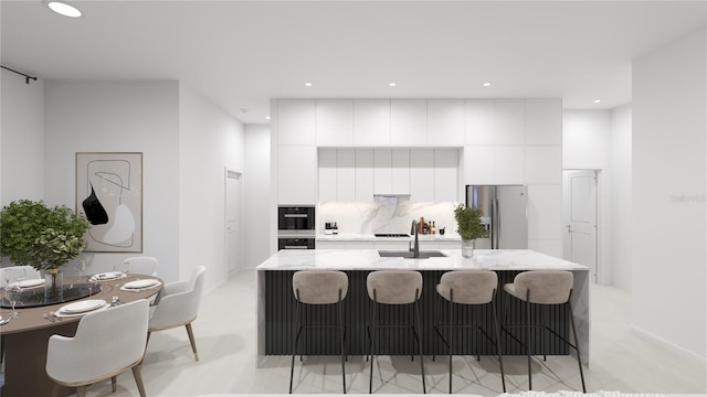 kitchen with white cabinetry, sink, stainless steel fridge, an island with sink, and decorative backsplash