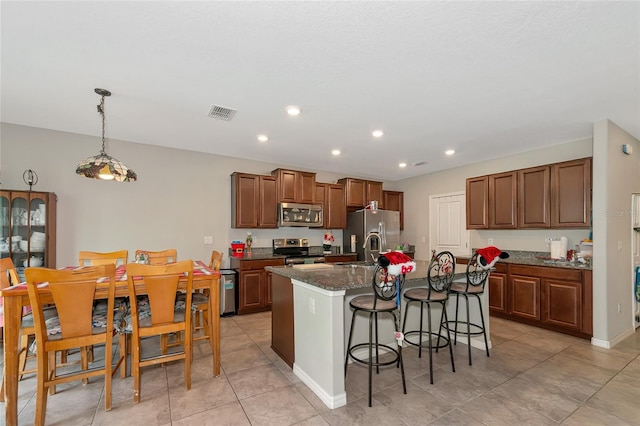 kitchen with dark stone countertops, a kitchen island with sink, a breakfast bar area, stainless steel appliances, and decorative light fixtures