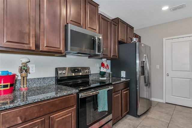 kitchen featuring stainless steel appliances, dark stone counters, light tile patterned flooring, and dark brown cabinets