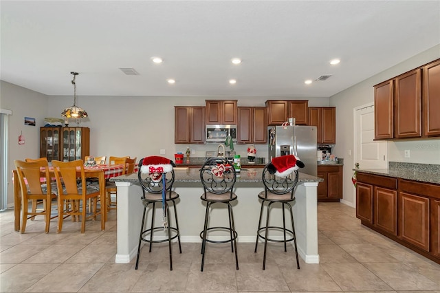 kitchen with decorative light fixtures, stainless steel appliances, a center island with sink, and a kitchen bar