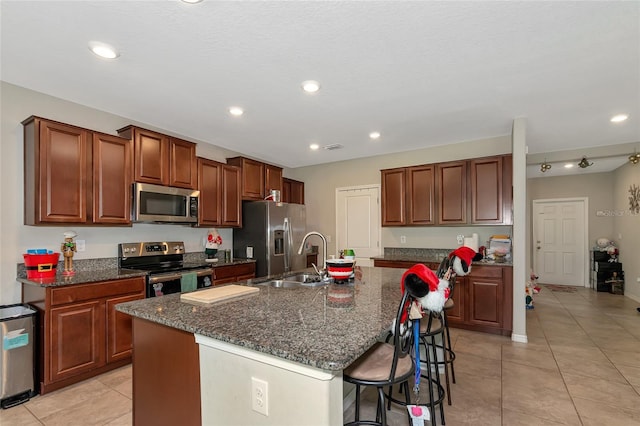 kitchen featuring stainless steel appliances, sink, light tile patterned flooring, an island with sink, and a breakfast bar