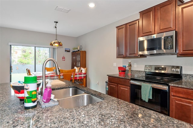 kitchen with decorative light fixtures, stainless steel appliances, dark stone countertops, and sink