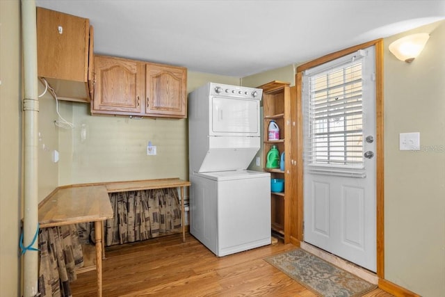 laundry room featuring cabinets, light hardwood / wood-style floors, and stacked washer and clothes dryer