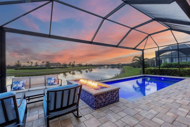 pool at dusk with a patio, a water view, glass enclosure, and an outdoor living space with a fire pit