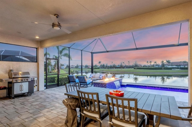 patio terrace at dusk with a lanai, ceiling fan, a water view, a fire pit, and grilling area