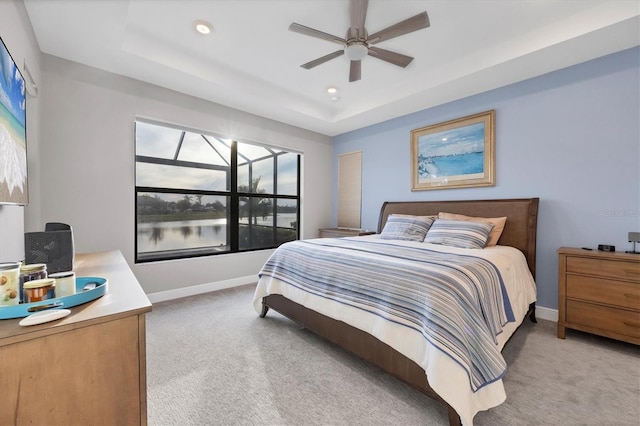 carpeted bedroom with ceiling fan and a tray ceiling