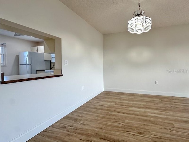 unfurnished dining area featuring light hardwood / wood-style flooring, a textured ceiling, and a notable chandelier