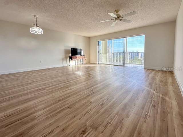 unfurnished living room with ceiling fan with notable chandelier, a textured ceiling, and light wood-type flooring