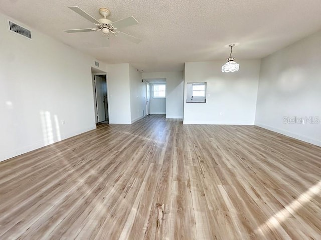 spare room with ceiling fan with notable chandelier, a textured ceiling, and light wood-type flooring