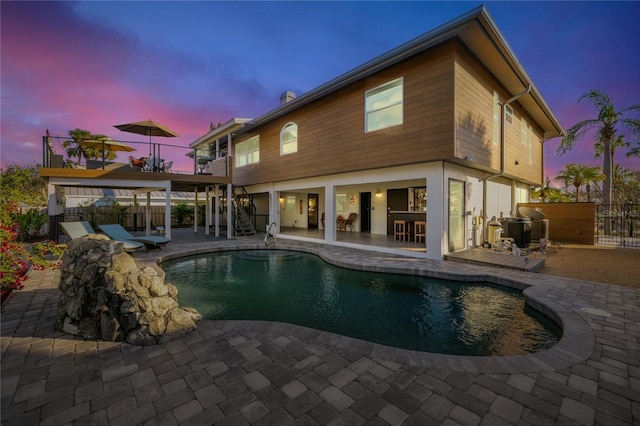 pool at dusk featuring a bar, central AC, and a patio area